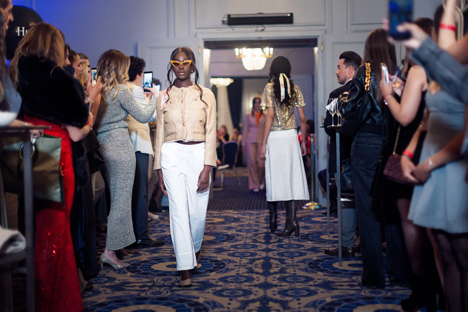 Model in a gold jacket walking between guests